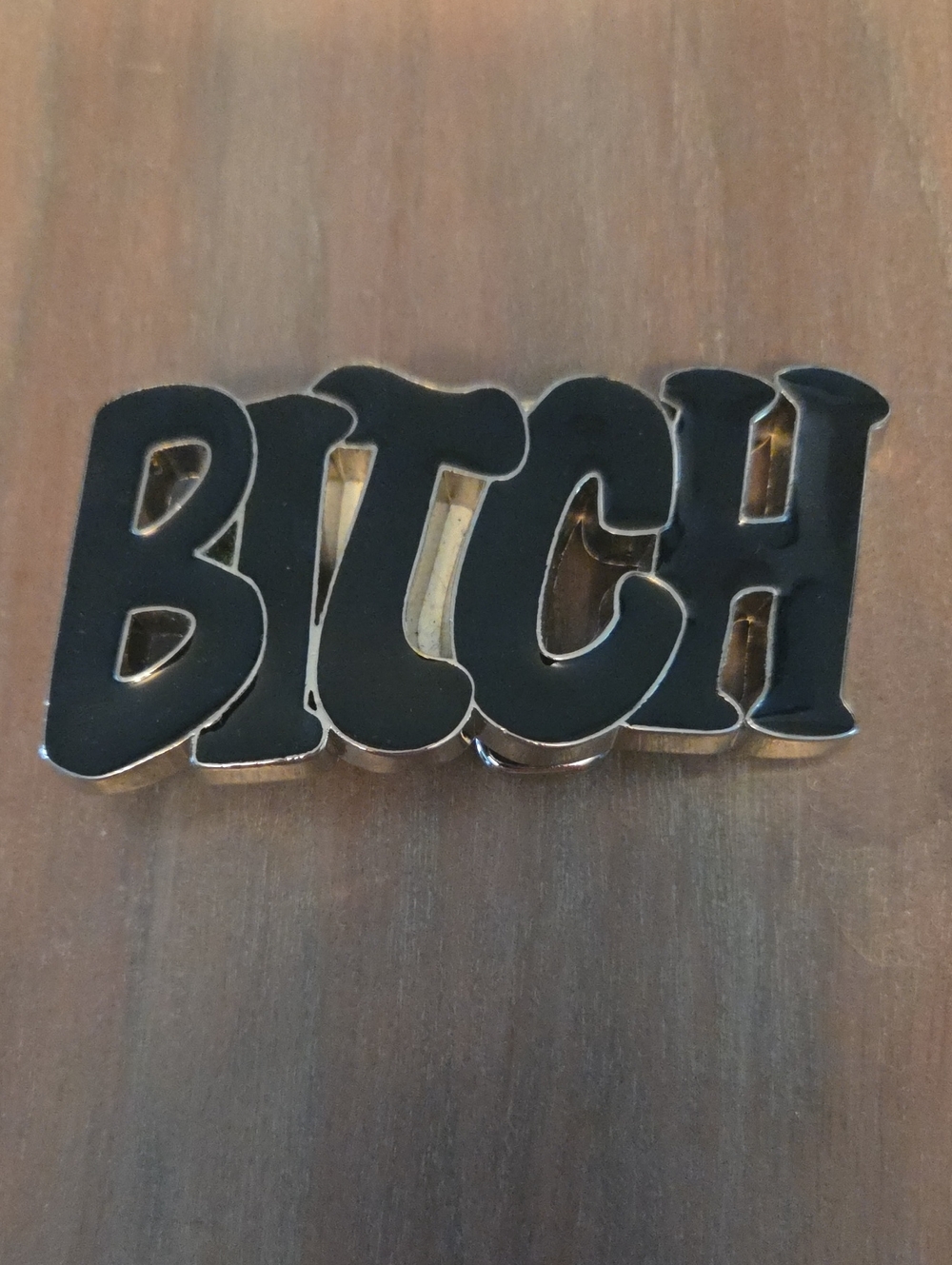 belt buckle featuring bold, black bubble letters with a polished metallic trim